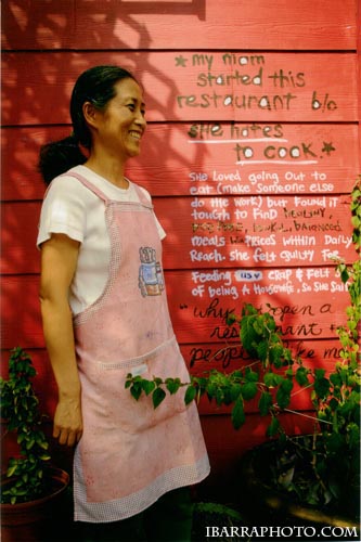 Koriente's founder standing on the restaurant patio beside the hand-written story on the red wall